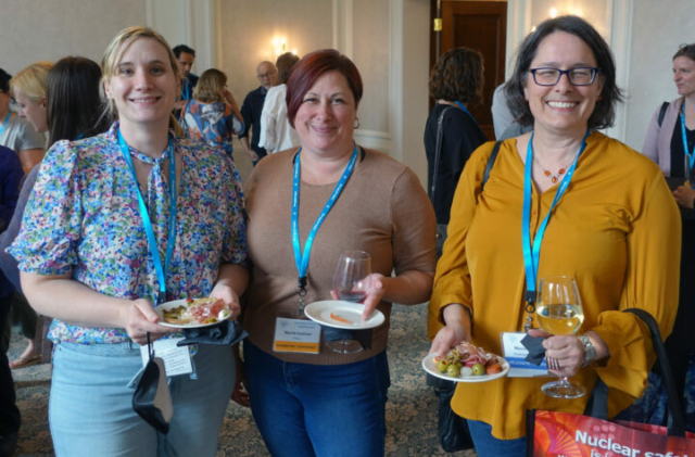 From left to right: Leah Shuparski-Miller, Marnie Sullivan, and Manon Rouleau. Crowd at a reception with food and drinks. Three women standing next to each other looking at the camera.