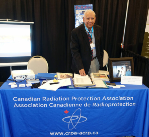 Our long-time CRPA archivist, Sunil Choubal, manning the archives booth. So much CRPA history to check out! A man stands behind a table with a blue table cloth with the CRPA logo on it. There are photos and documents on the table.