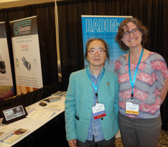 Jing Chen and Pam Warkentin Tow women stand next to a trade show booth.