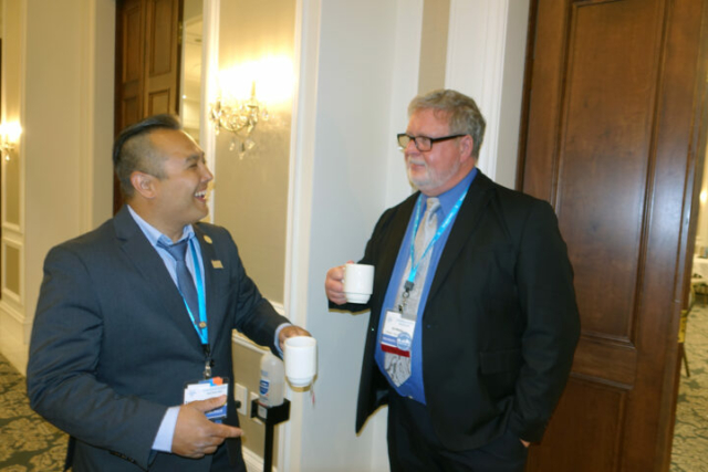 Francis Arnaldo and Ed Waller. Two men stand next to an open door. They are holding coffee cups and laughing.