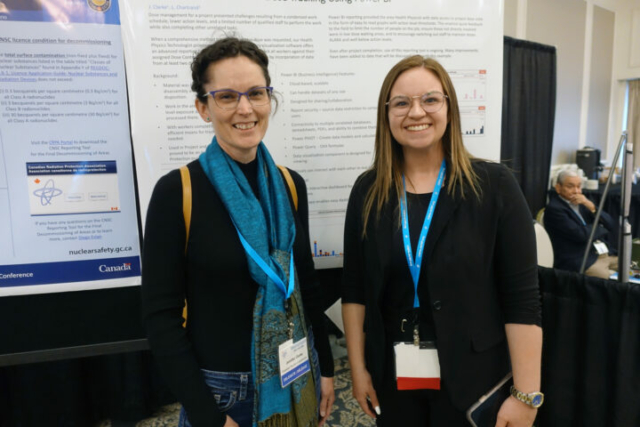 Jennifer Clarke and Brittany Cole. Two women stand next to each other and smiling at the camera. There is a conference poster hanging behind them.