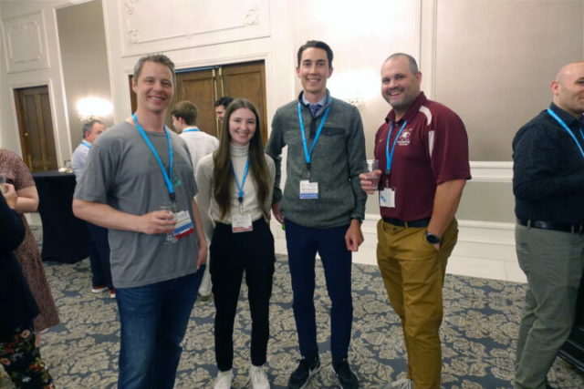 From left to right: Mike Stoicescu, Alicia Douglas, Ryan Cooke, and Chris Malcolmson. four people standing side-by-side and smiling at the camera. There is a reception crowd behind them.