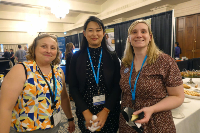 From left to right: Diana Moscu, Haiqian Ma, and Leah Shuparski-Miller. Three women stand next to each other and smiling at the camera. There is a reception crown behind them.