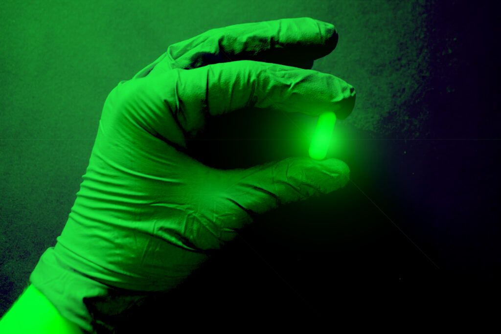 Green radioactive capsule in a gloved hand.