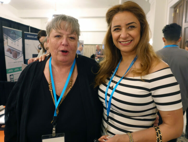 Sue Singer (secretariat) and Mojgan Soleimani (treasurer) two women stand with their arms around each other and smile at the camera.