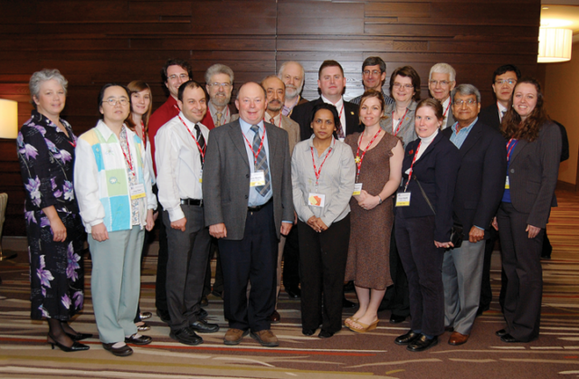 A photo from the CRPA conference in Ottawa, ON, in 2010. From left to right: Lois Sowden-Plunkett, Jing Chen, Leah Shuparski-Miller, Dave Niven, Ali Shoustarian, Bliss Tracy, Kevin Bundy, Anar Baweja, Gary Kramer, Jahan Quaji, Chris Clement, Jodie Ploquin, Roger Hugron, Liz Krivonosov, Tanya Hewitt, Richard Osborne, Din Lal, Chunsheng Li, and Julie Burtt. A group of people standing to face the camera. They are wearing business attire and laniards.