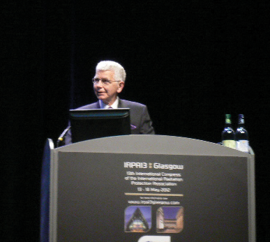 Richard Osborne opened the IRPA13 scientific program py presenting his Sievert Lecture, “Story of Tritium.” A grey haired man wearing a suit and tie stands behind a podium with a sign on the front of it that says IRPA13 Glasgow
